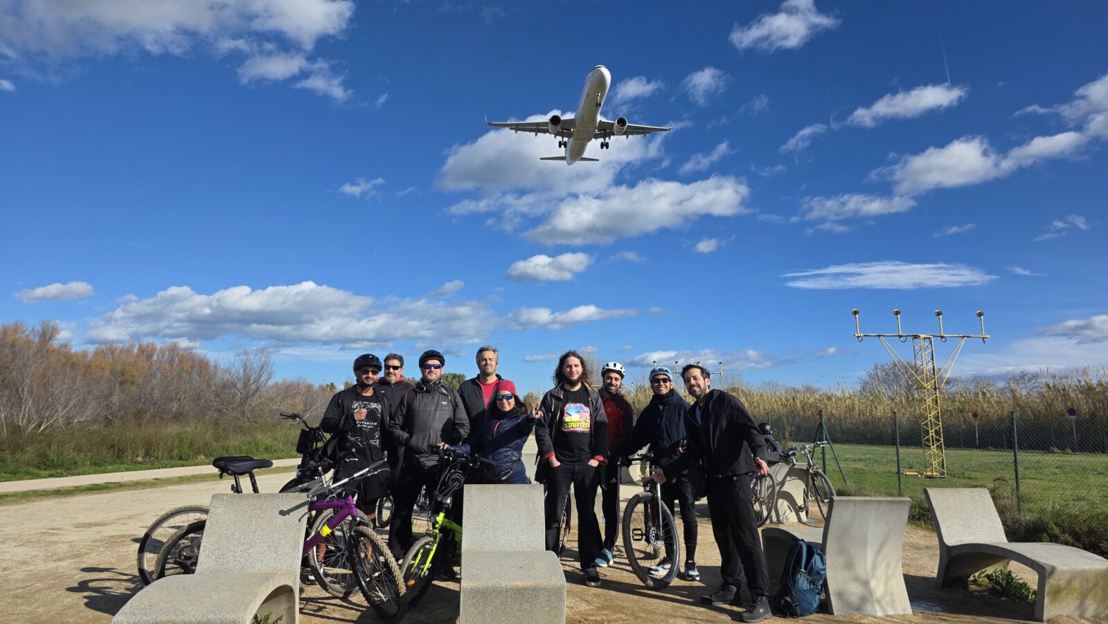International group with bicycles during an outdoor meetup in Barcelona with a plane flying overhead
